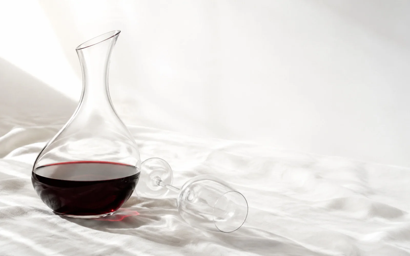 Karaffe mit Rotwein und ein liegendes Weinglas auf weißem Leinen